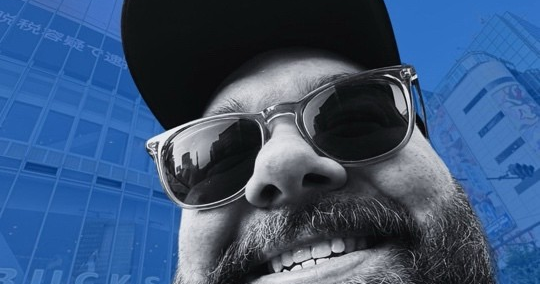 Matthew Banther wearing sunglasses against a blue city background.
